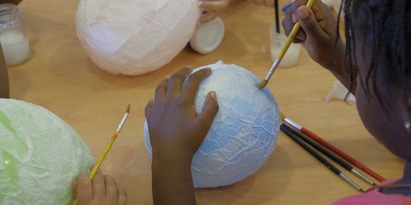 Un niño cubre un globito con papel mache