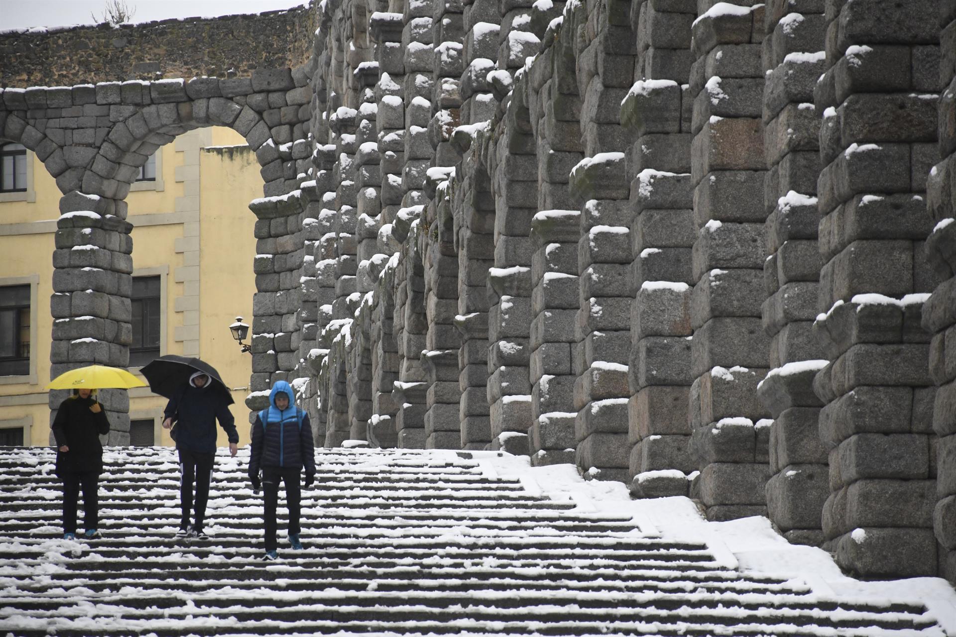 Varias personas caminan junto al acueducto de Segovia que este miércoles ha amanecido cubierto de nieve. . EFE/ Pablo Martin
