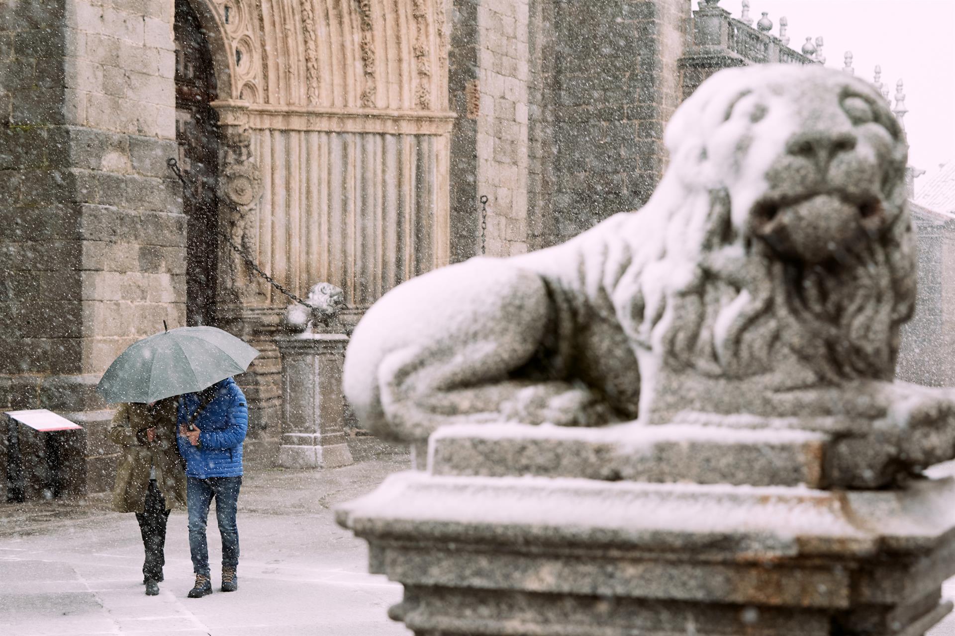 Dos personas se protegen de la nieve junto a los leones de la catedral de Ávila este miércoles. EFE/ Raúl Sanchidrián
