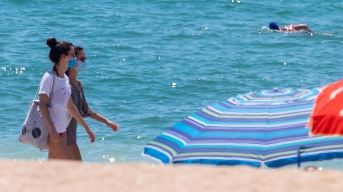 Dos jóvenes pasean con la mascarilla puesta por la orilla de la playa. EFE/Julián Pérez
