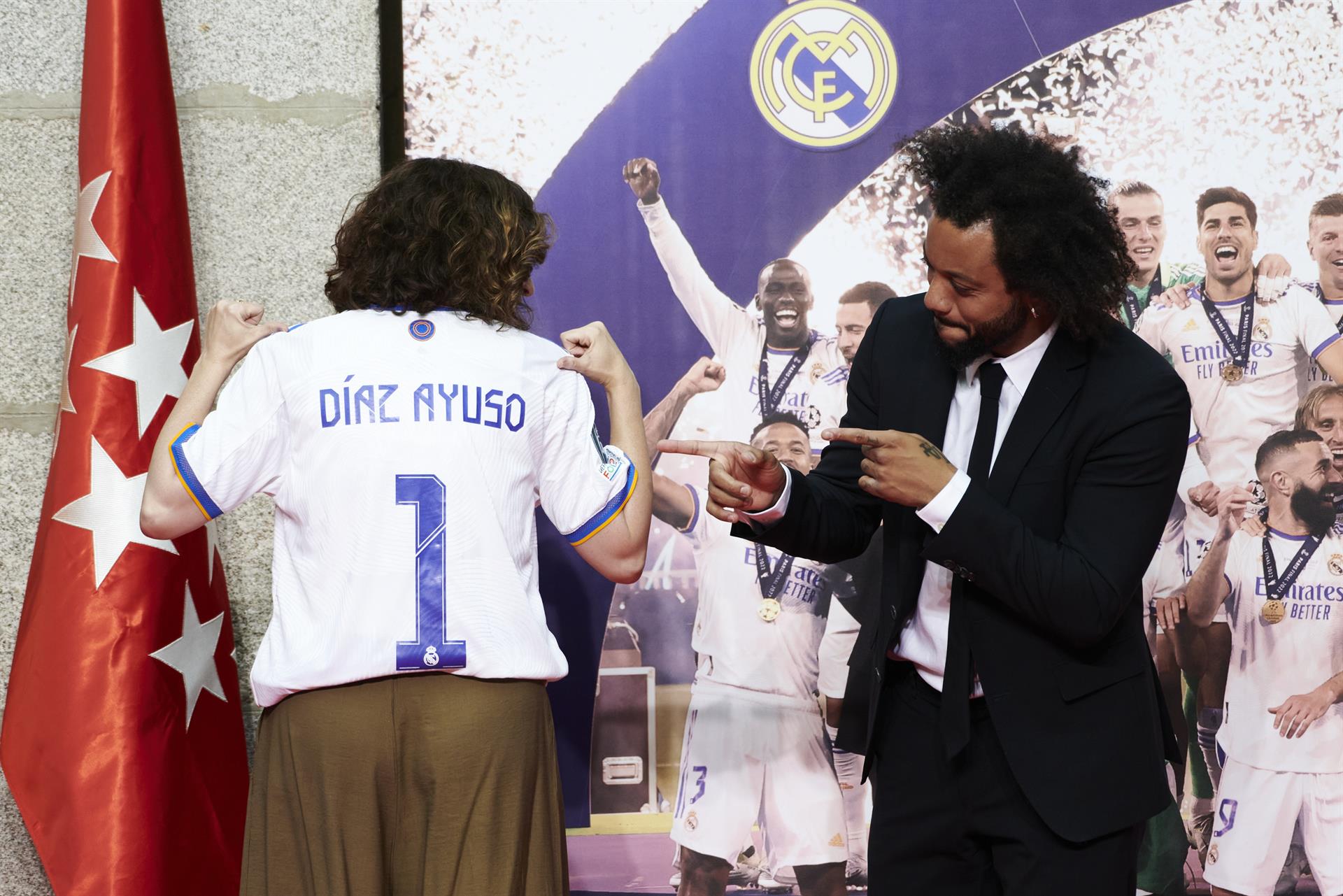 La presidenta de la Comunidad de Madrid, Isabel Díaz Ayuso (d), tras recibir una camiseta con su nombre de manos del capitán del Real Madrid, Marcelo Vieira, durante la recepción que ha tenido lugar este domingo la Real Casa de Correos, una de las paradas del recorrido realizado esta tarde por el equipo para celebrar su victoria en la final de la Liga de Campeones. EFE/Luca Piergiovanni
