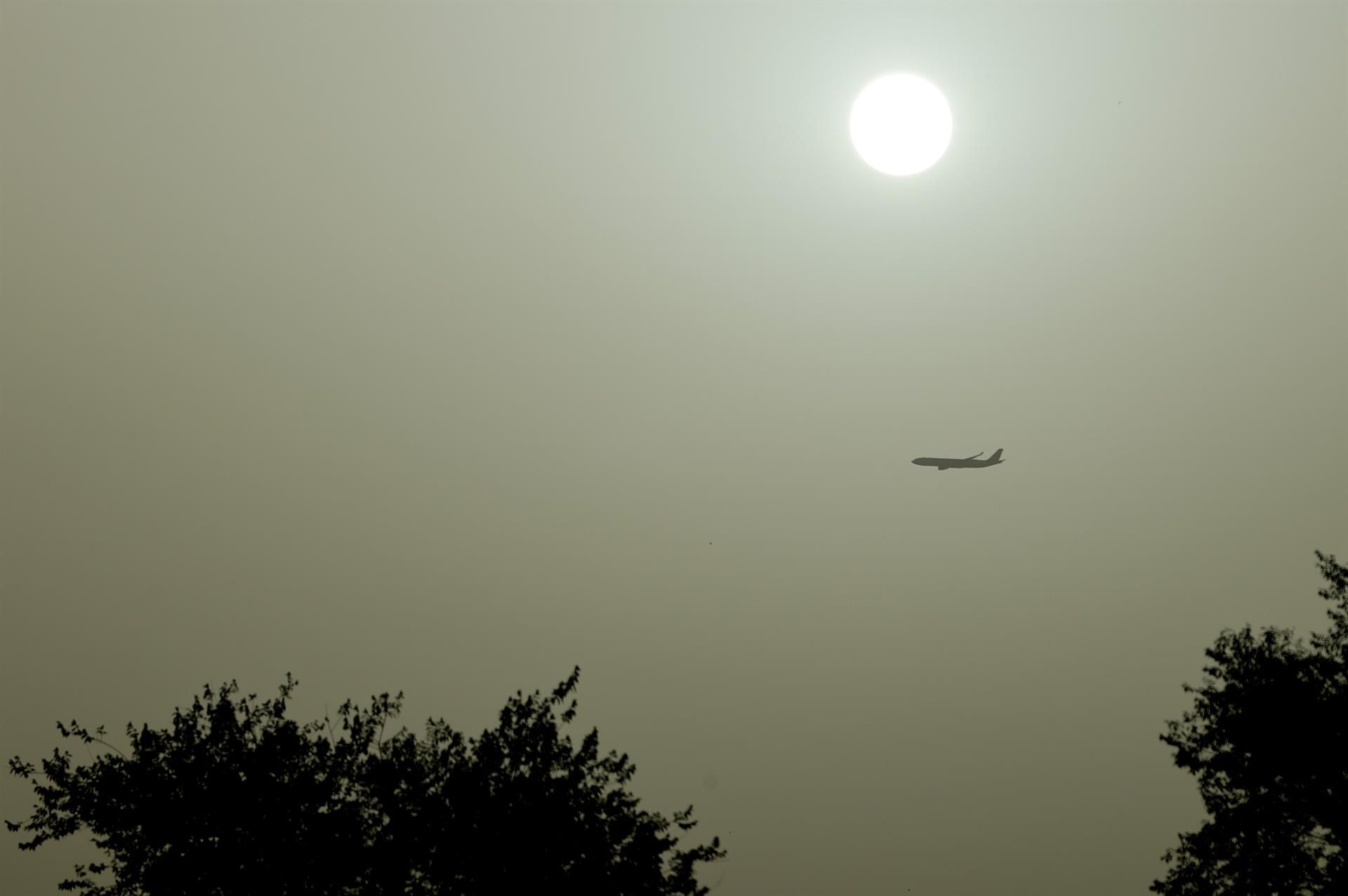 Un avión pasa bajo un sol mortecino que se recorta sobre la calima cuando continúa la ola de calor en la mayor parte del país. EFE/ Mariscal
