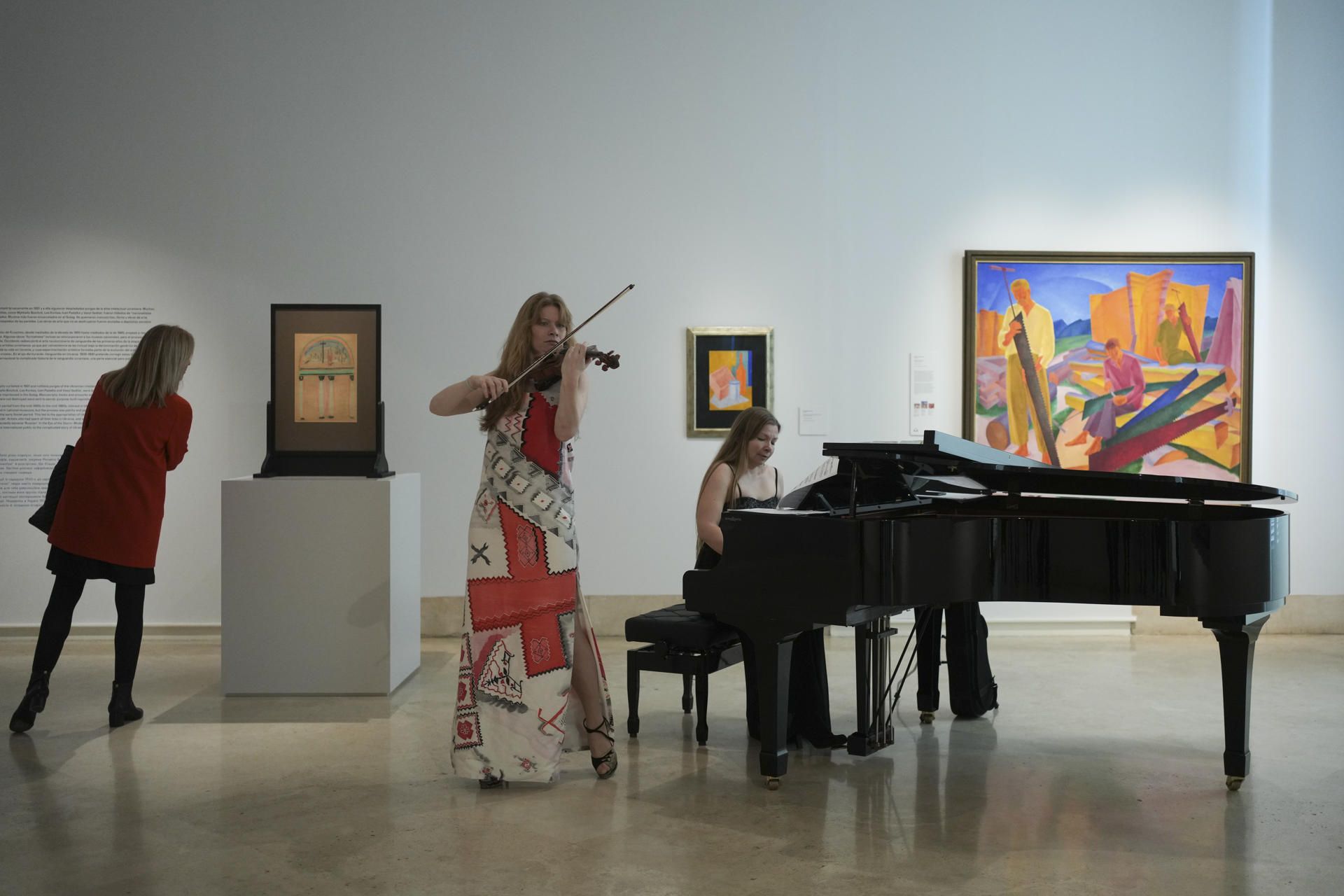 Dos intérpretes tocan una melodía cerca de algunas de las obras expuestas en el marco de la exposición  "En el ojo del huracán. Vanguardia en Ucrania, 1900-1930", durante su presentación en el Museo Nacional Thyssen-Bornemisza, este lunes, en Madrid. EFE/ Borja Sánchez Trillo
