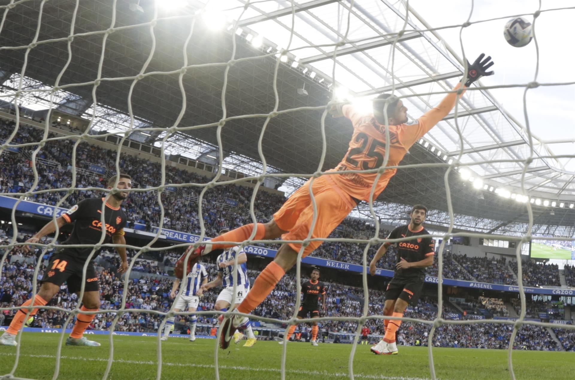 El portero del Valencia, Giorgi Mamardashv (c), despeja un balón durante el partido correspondiente a la decimotercera jornada de LaLiga entre Real Sociedad y Valencia CF disputado este domingo en el Reale Arena de San Sebastián. EFE/ Javier Etxezarreta
