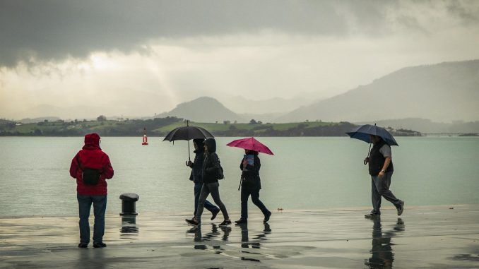 Gente pasea bajo la lluvia junto a la bahía de Santander este viernes donde se han registrado lluvias y descenso de temperaturas. EFE/ Román G. Aguilera
