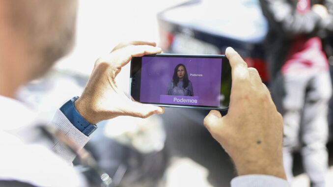 Un hombre observa en su móvil la imagen de la secretaria general de Podemos, Ione Belarra durante la rueda de prensa celebrada este viernes en la sede del partido en Madrid donde ha anunciado que Podemos concurrirá a las elecciones generales del 23 de julio con la coalición de Sumar. EFE/Rodrigo Jiménez
