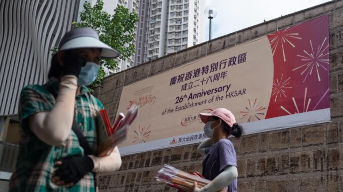 Dos personas pasan delante de una pancarta que celebra el 26 aniversario del traspaso en Hong Kon a China. EFE/EPA/BERTHA WANG
