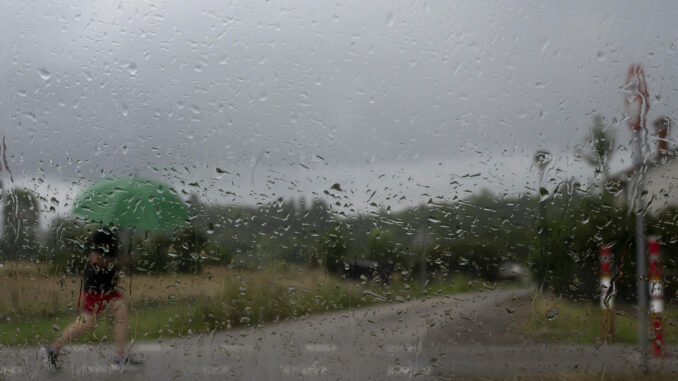 Vista a través de un cristal de un hombre que camina este jueves bajo la lluvia en una calle en la localidad cántabra de Hinojedo. EFE/Pedro Puente Hoyos