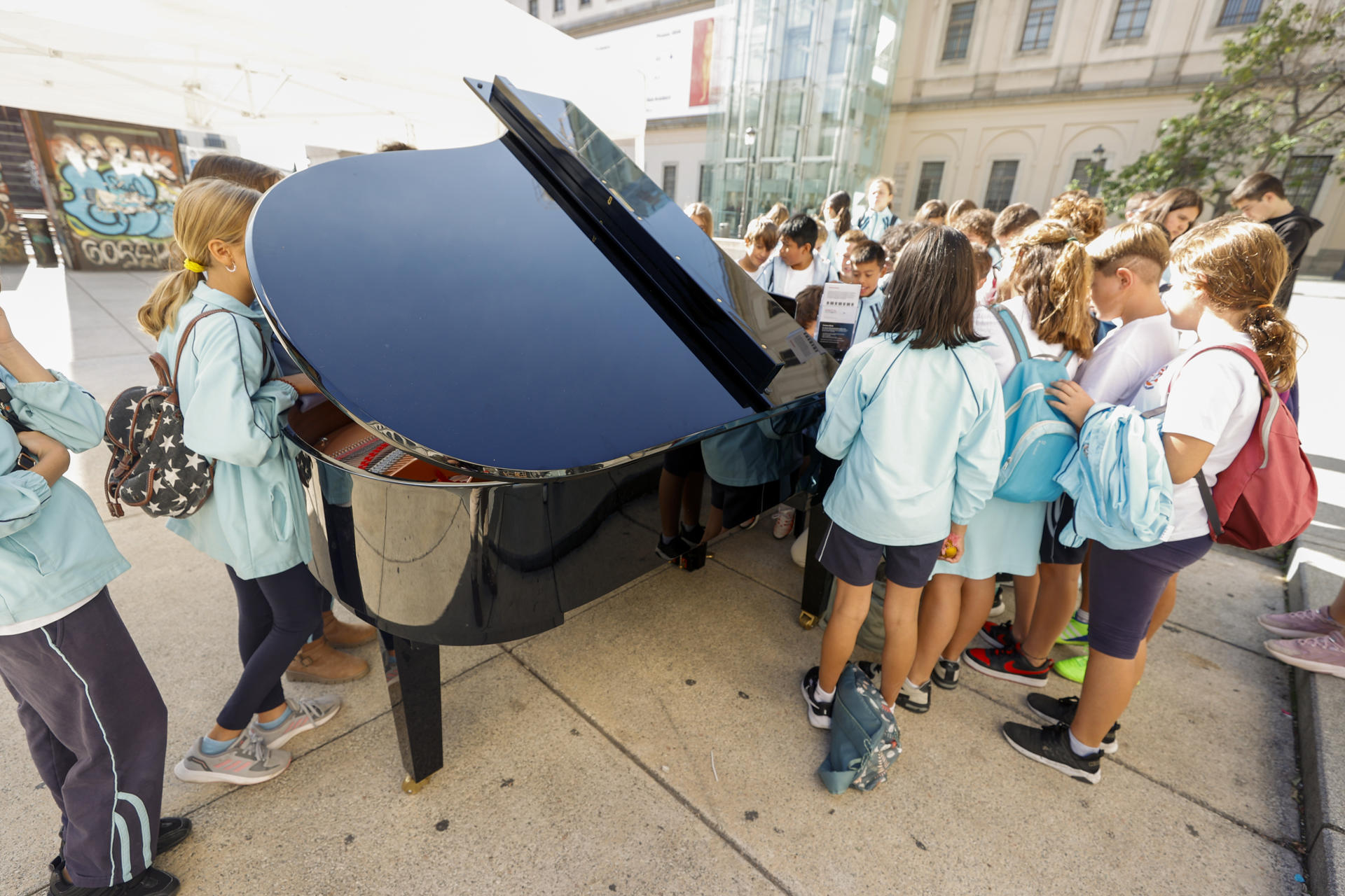 Varios niños tocan un piano de cola en la Plaza del Museo Reina Sofía en Madrid este viernes durante la iniciativa Pianos por Madrid. EFE/ Javier Lizón
