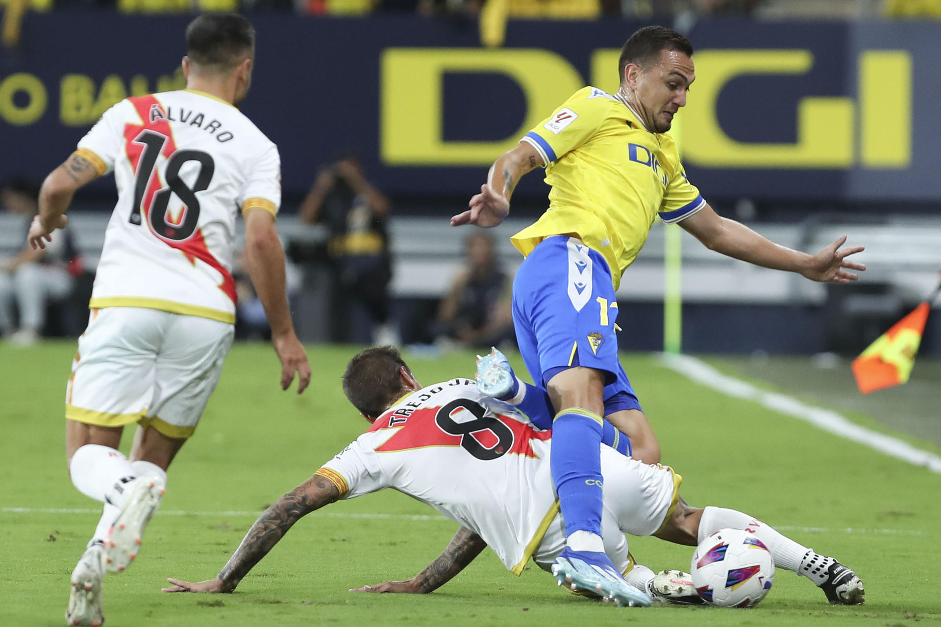 El delantero del Rayo Vallecano Trejo (en el suelo) lucha por el balón con el centrocampista del Cádiz CF Gonzalo Escalante (d) durante el partido de LaLiga que enfrenta al Cádiz CF y al Rayo Vallecano este miércoles en el estadio Nuevo Mirandilla. EFE/Román Ríos
