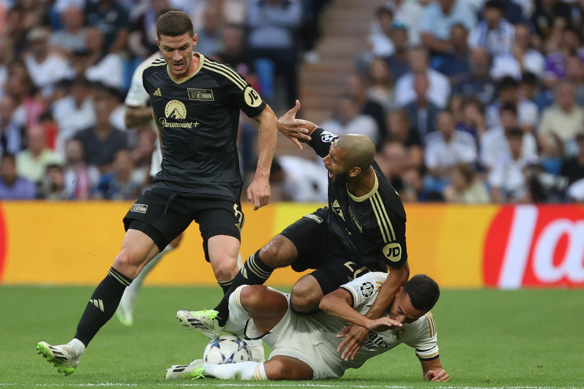 El centrocampista francés del Unión Berlín, Aissa Laidouni (c), cae ante la entrada del centrocampista Real Madrid, Lucas Vázquez, durante el encuentro correspondiente a la fase de grupos de la Liga de Campeones que disputan hoy miércoles en el estadio Santiago Bernabéu, en Madrid. EFE / Kiko Huesca.
