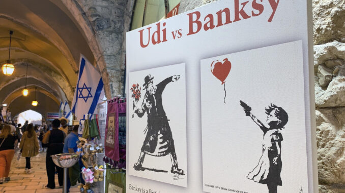 Un cartel muestra las obras "No les den armas para que no tengamos que construir un muro, y se encontrarán con flores" del pintor israelí Udi Merioz, en contraposición a la obra del artista Banksy, "Niña con globo", en Jerusalén este viernes. EFE/ Yemeli Ortega
