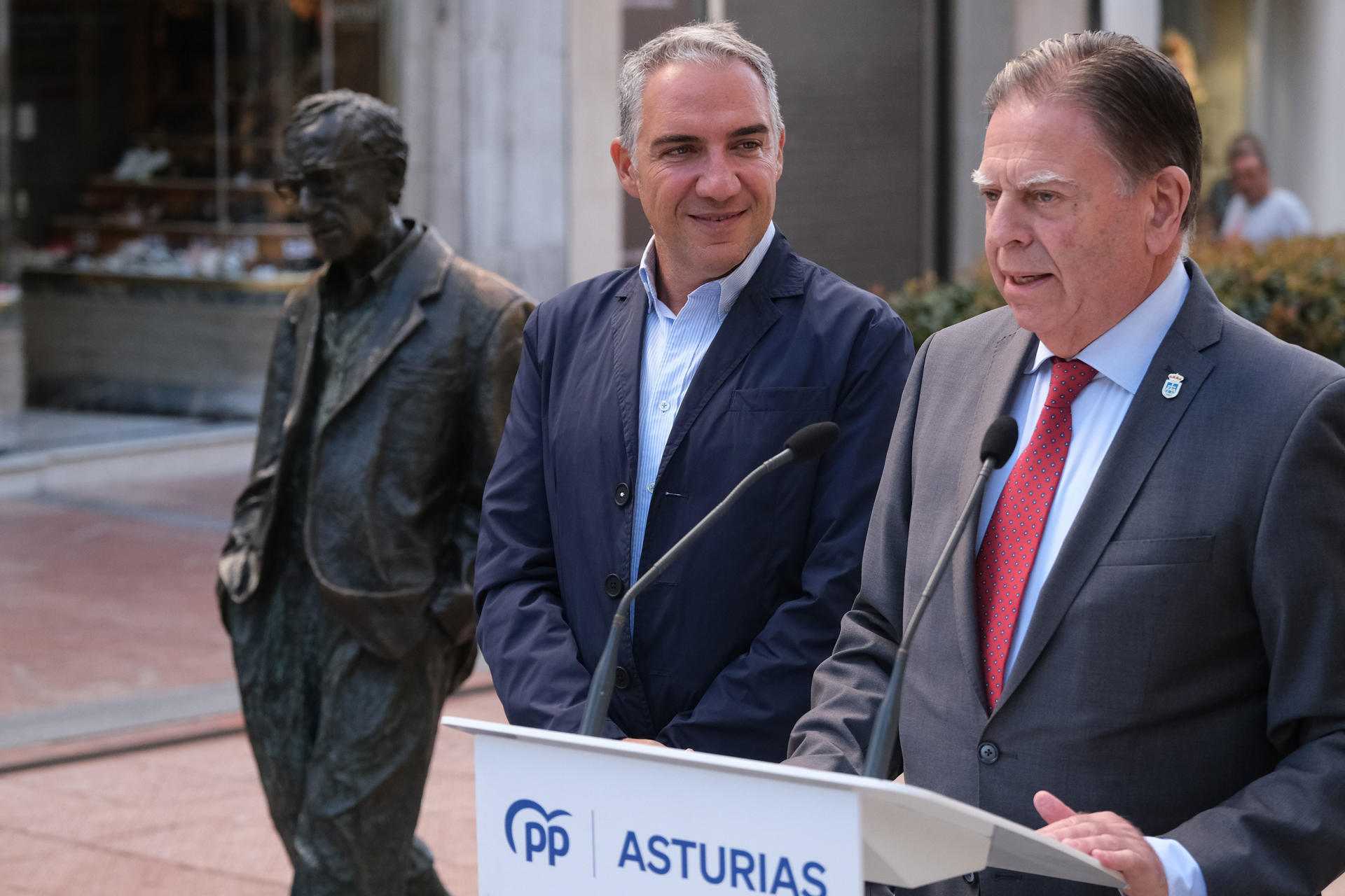 El coordinador general del PP, Elías Bendodo(c), atiende a los medios junto al alcalde de Oviedo, Alfredo Canteli (d), junto a la estatua de Woody Allen, este domingo en Oviedo. EFE/Paco Paredes
