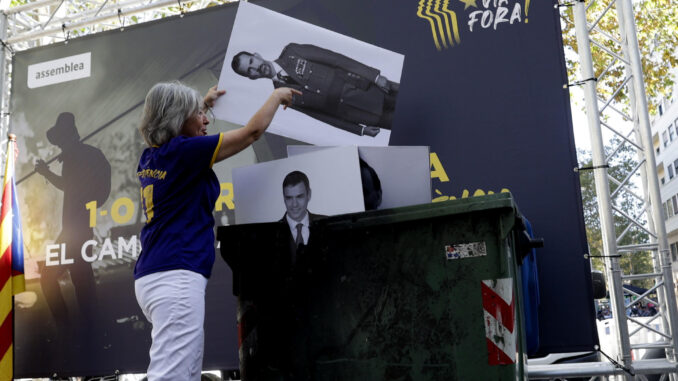 La presidenta de la ANC, Dolors Feliu, tira a un contenedor un retrato de Felipe VI junto a otro del presidente del Gobierno en funciones, Pedro Sánchez, durante un acto organizado por la Asamblea Nacional Catalana para conmemorar el sexto aniversario del 1 de octubre de 2017, este domingo en Barcelona. EFE/ Quique García
