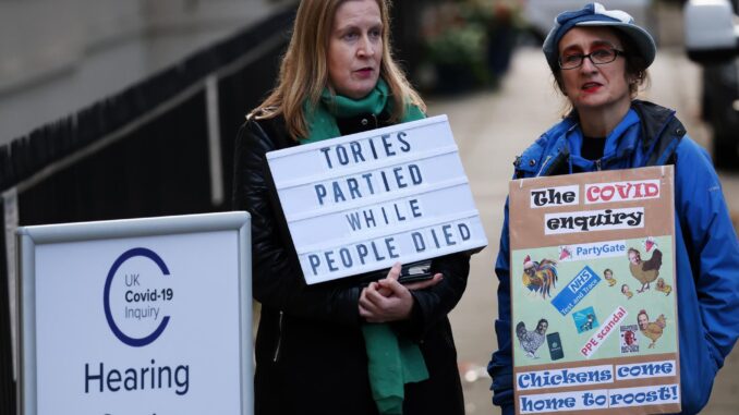 Varias personas protestan frente al lugar donde se lleva una investigación sobre la gestión de la pandemia de coronavirus por parte del exprimer ministro británico boris Johnson. EFE/EPA/Andy Rain
