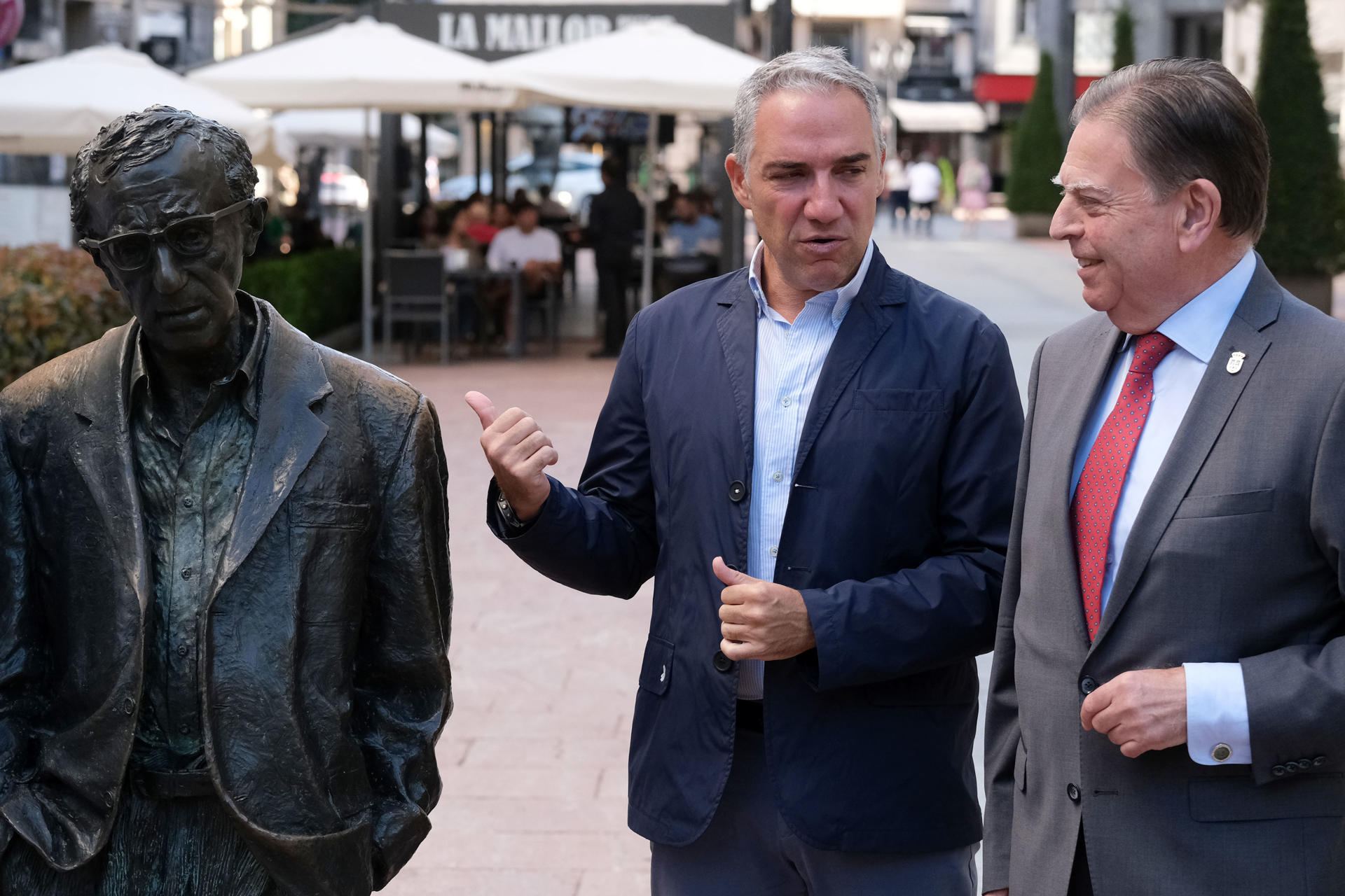 El coordinador general del PP, Elías Bendodo(c), atiende a los medios junto al alcalde de Oviedo, Alfredo Canteli (d), mientras ambos posan con la estatua de Woody Allen, este domingo en Oviedo. EFE/Paco Paredes
