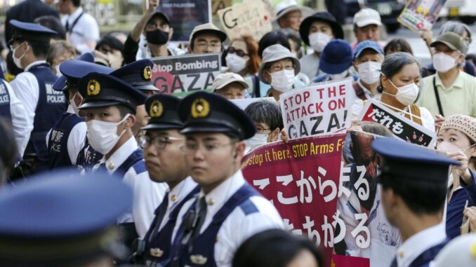 Agentes de policía vigilan mientras manifestantes con pancartas en solidaridad con el pueblo palestino protestan contra "la masacre de Israel en Gaza" y el comercio de armas, cerca de la Iikura Guest House del Ministerio de Exteriores en Tokio, donde se celebra una reunión de ministros de Exteriores del G7, el 7 de noviembre de 2023. EFE/EPA/KIMIMASA MAYAMA
