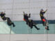 Varios bomberos saludan mientras descienden por una cuerda desde el tejado del Hospital Puerta de Hierro durante una demostración previa a la entrega de regalos a los niños ingresados en el centro médico, en Majadahonda, Madrid, este viernes. EFE/Sergio Pérez