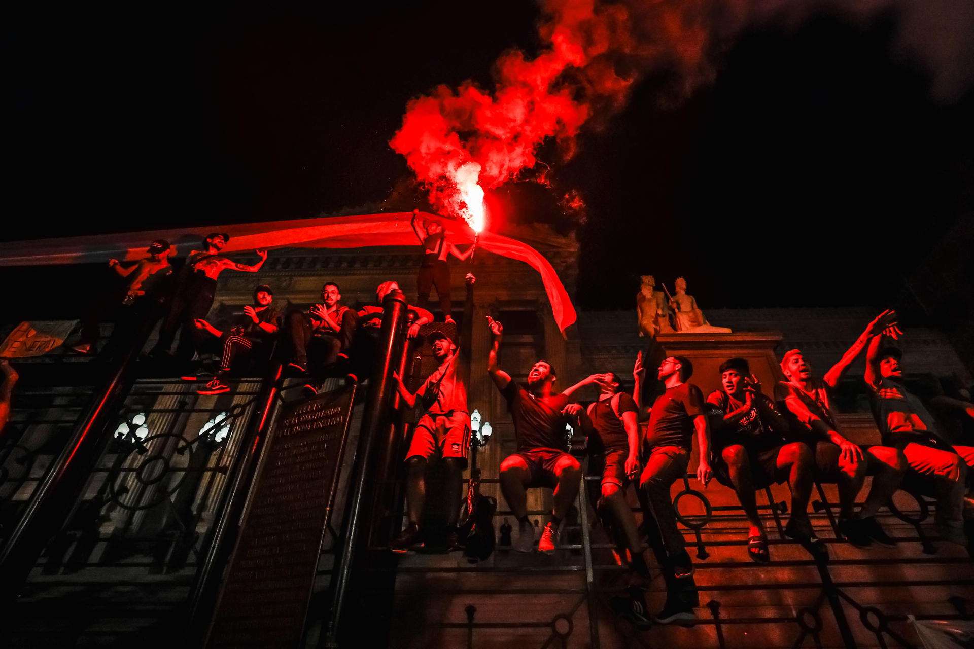 Varias personas encienden una bengala trepados sobre una reja exterior en la sede del Congreso, durante una manifestación contra las medidas anunciadas por el presidente Javier Milei, que empezó en la noche de este miércoles y se extendió hasta la madrugada de hoy, frente al Congreso de la Nación en Buenos Aires (Argentina). EFE/ Juan Ignacio Roncoroni
