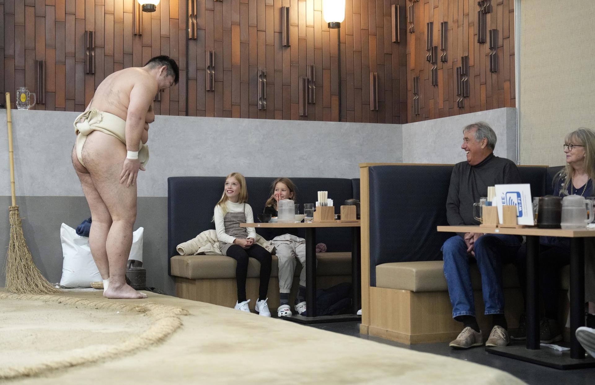 El ex luchador de sumo Jokoryu interactúa con jóvenes turistas extranjeros durante un almuerzo con espectáculo de sumo en el restaurante Yokozuna Tonkatsu Dosukoi Tanaka, en Tokio. EFE/EPA/FRANCK ROBICHON
