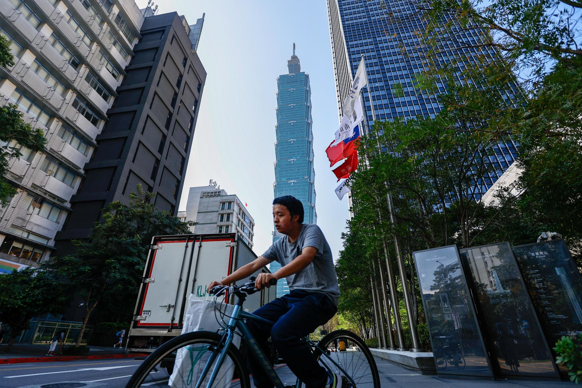 Un ciclista circula junto a una bandera de Taiwán en una calle desde la que se ve el rascacielos Taipei 101, el 12 de enero de 2024, un día antes de las elecciones presidenciales. EFE/EPA/DANIEL CENG
