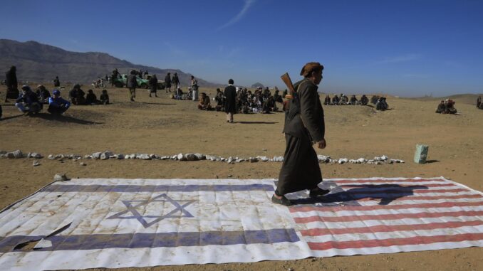 Un integrante de una tribu leal a los hutíes camina encima de las banderas de Israel y Estados Unidos durante un encuentro para combatientes recientemente reclutados el 22 de enero en las afueras de Saná. EFE/YAHYA ARHAB
