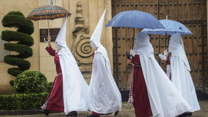 Unos nazarenos de la Hermandad de La Sentencia se protegen de la lluvia con paraguas mientras caminan hacia su templo en Córdoba (Andalucía). EFE/ Rafa Alcaide
