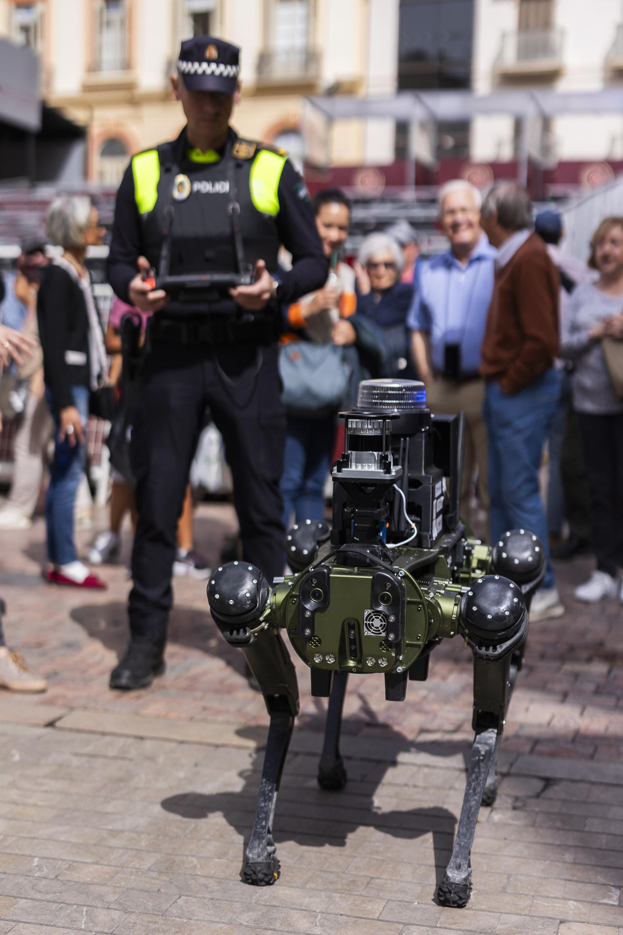 Un agente de la Policía Local de Málaga realiza una demostración práctica este martes en la calle Marqués de Larios de la capital malagueña de un robots cuadrúpedo que ha diseñado la Universidad (UMA) y que pueden patrullar con los municipales. EFE/Carlos Díaz
