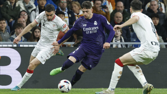 El centrocampista uruguayo del Real Madrid Fede Valverde (c) dirige el balón ante la defensa del Athletic de Bilbao, durante el partido de la jornada 30 de LaLiga que Real Madrid y Athletic Club de Bilbao disputaron en el estadio Santiago Bernabéu, en Madrid. EFE/ Chema Moya
