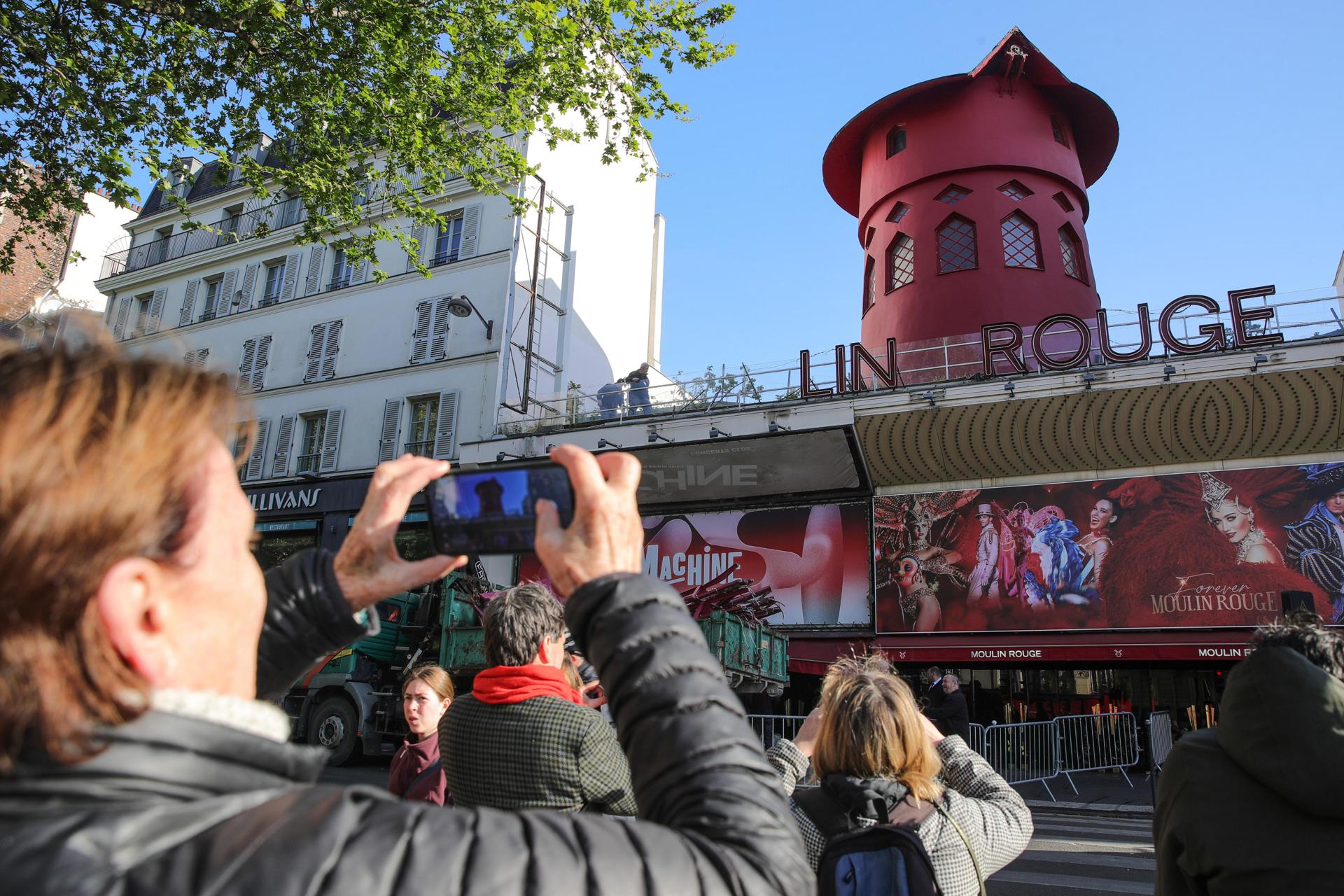 La gente se detiene para tomar fotos de la fachada del Moulin Rouge sin sus alas en París, Francia, 25 de abril de 2024. Durante la noche del 24 al 25 de abril, las aspas del Moulin Rouge se derrumbaron sin causar víctimas, según fuentes oficiales. (Francia) EFE/EPA/Teresa Suárez
