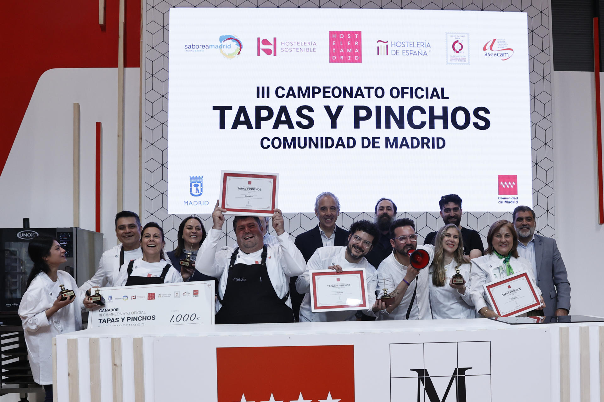 José Antonio Aparicio (c, detrás), presidente de Hostelería Madrid, posa con Antonio María Ventura (3i) y Raquel Cuevas (5i), campeones del III Campeonato Oficial de Tapas y Pinchos de la Comunidad de Madrid, organizado por Hostelería Madrid, y con el resto de participantes durante la tercera jornada de la 37 edición de la feria Salón Gourmets este miércoles en Madrid. EFE/ Fernando Alvarado
