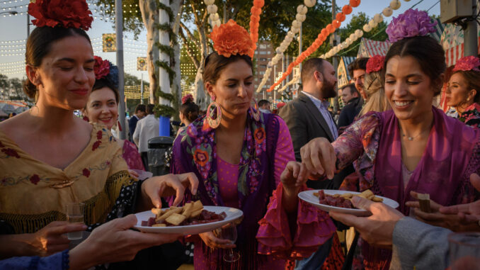 Varias mujeres vestidas de gitana toman chacinas en el Real de la Feria de Abril de Sevilla este lunes. EFE/ Raúl Caro

