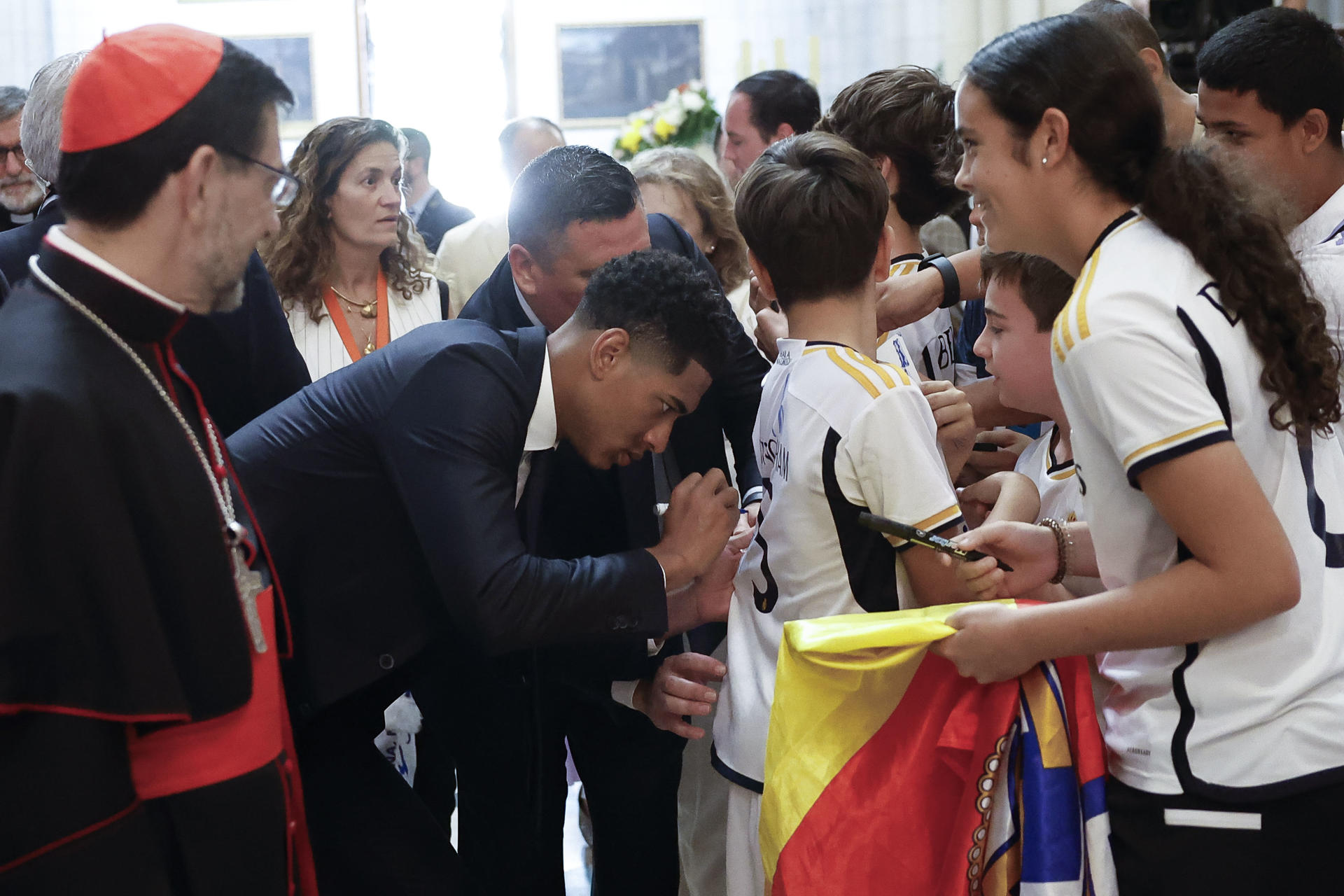El centrocampista británico del Real Madrid Jude Bellingham firma un autógrafo a un niño en la Catedral de la Almudena, primera parada del recorrido realizado este domingo por el equipo para celebrar su victoria en la final de la Liga de Campeones. EFE/Chema Moya POOL
