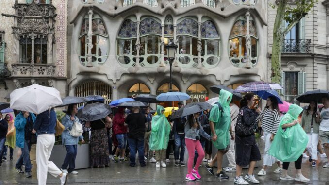 Fotografía de archivo de varios turistas protegiéndose de la lluvia en las inmediaciones de la Casa Batlló del paseo de Gracia de Barcelona.EFE/ Enric Fontcuberta
