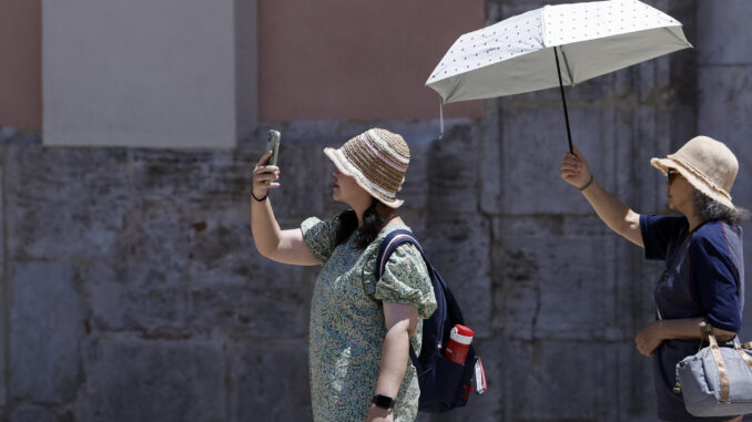 Dos turistas sen protegen del sol y del calor con un parasol durante la mañana de este martes en Valencia. EFE/Kai Försterling
