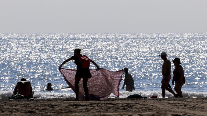 Una persona despliega una tela a la orilla en la playa de la Malvarrosa aprovechando las temperaturas veraniegas y el cielo despejado de estos primeros días de julio. EFE/Kai Försterling
