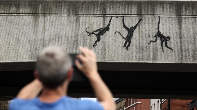 Un hombre toma fotografías de la nueva obra de arte de Banksy que presenta monos en el costado de un puente ferroviario Overground en Shoreditch, al este de Londres, Gran Bretaña, el 8 de agosto de 2024. El artista británico Banksy lanzó el 7 de agosto en Londres una tercera obra de arte con temática animal en tres días. (Reino Unido, Londres) EFE/EPA/ANDY LLUVIA
