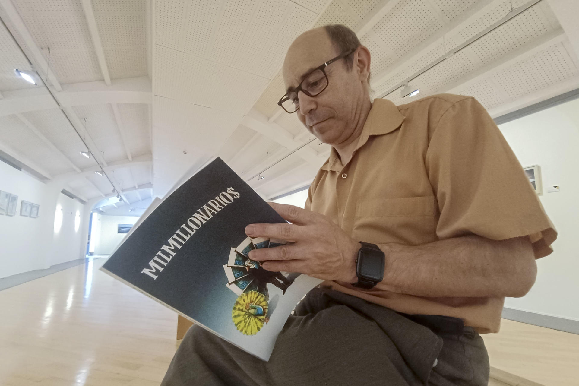 Juan García, comisario de la muestra, lee el catálogo de ‘Milmillonarios’, la exposición central de la XXXI Muestra Internacional de las Artes del Humor de Alcalá de Henares, en la que se representa a través de viñetas y el doble sentido la codicia, la opulencia, la avaricia y el descaro de los más pudientes. EFE/ Guilllermo Martínez
