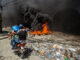 Dos hombres se movilizan en motocicleta frente a una barricada con fuego durante una protesta este lunes, en el barrio Solino, en Puerto Principe (Haití). EFE/ Mentor David Lorens