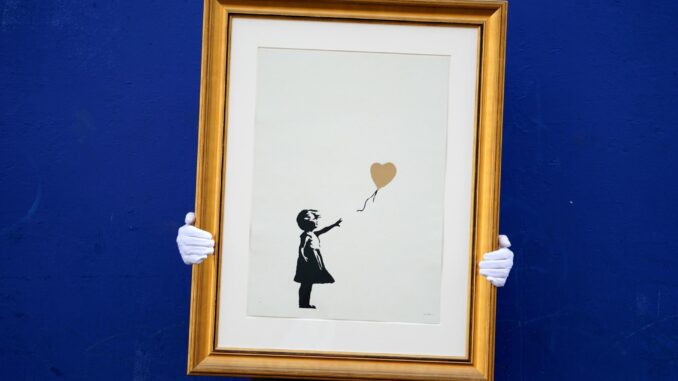 Imagen de Archivo de un empleado de la casa de subastas Christie's sosteniendo una versión de la obra "Niña con globo" del artista Banksy en Londres, Reino Unido.
 EFE/ Will Oliver
BRITAIN ARTS BANKSY:London (United Kingdom), 30/08/2019.- A Christie's employee poses with a print of the gold version of 'A Girl with Balloon' artwork by anonymous British street artist Banksy on the Southbank in Central London, Britain, 30 August 2019. Two versions of the artwork will be sold at a dedicated Christie's online sale of Banksy's work called 'Banksy: I can't believe you Morons actually buy this sh*t' from 11 to 24 September. (Reino Unido, Londres) EFE/EPA/WILL OLIVER
