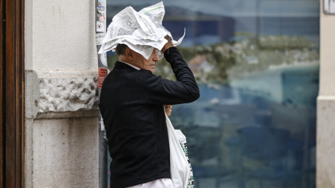 Un hombre trata de protegerse de la lluvia con unas hojas de periódico este jueves en València. EFE/Biel Aliño
