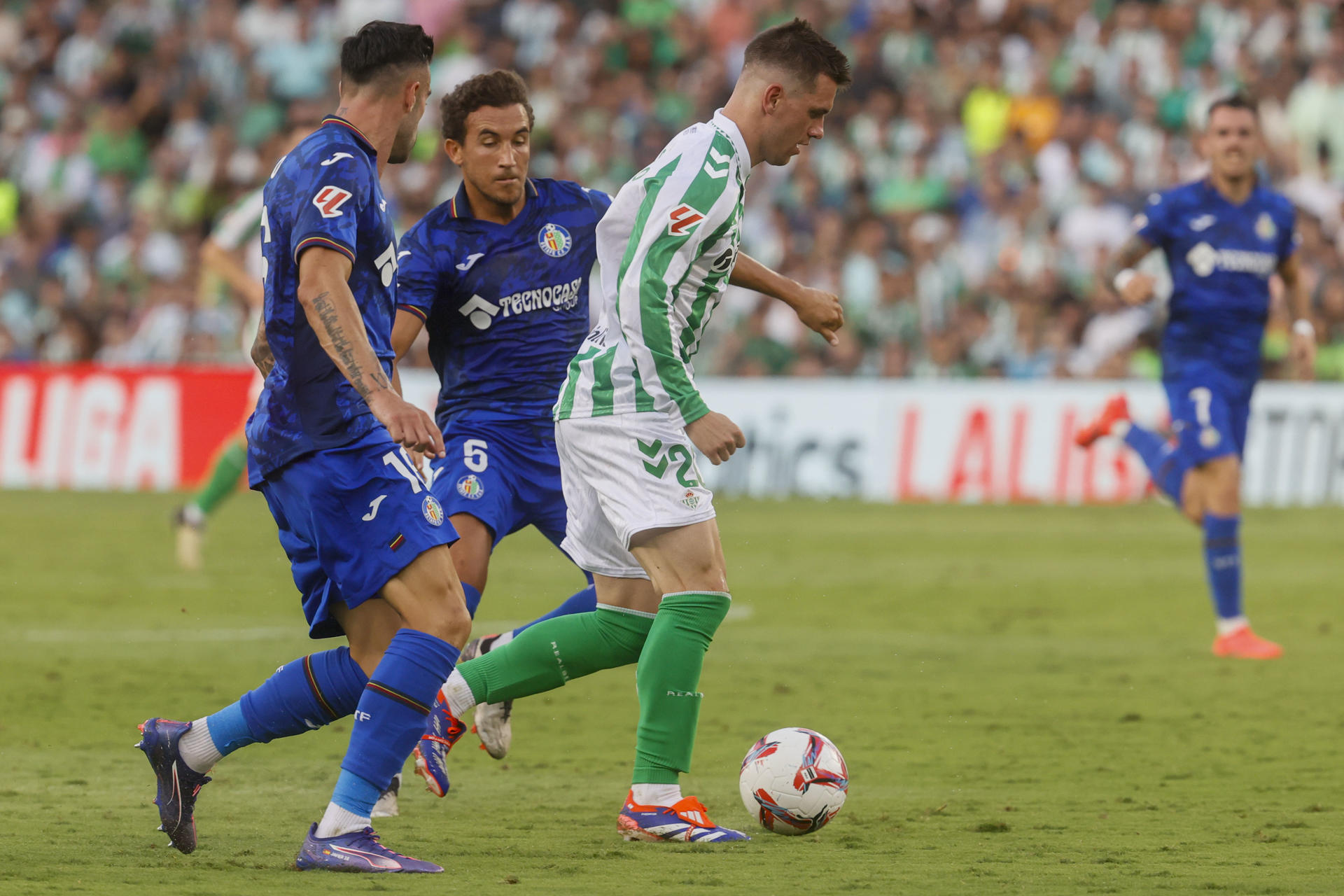 El centrocampista argentino-italiano del Betis Giovani Lo Celso (d) disputa un balón con el centrocampista español del Getafe Luis Milla (c) durante el partido de la jornada 3 de LaLiga, en el estadio Benito Villamarín de Sevilla. EFE/ José Manuel Vidal
