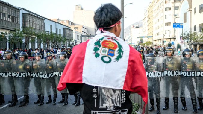 Un manifestante sostiene una bandera de Perú frente a miembros de la policía durante una protesta cerca al Congreso de la República este jueves, en Lima (Perú). EFE/ STR
