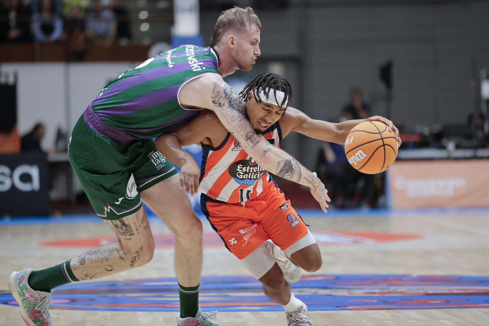 El base estadounidense del Coruña, Brandon Taylor (d), juega un balón con Olek Balcerowsky, de Unicaja, durante el encuentro correspondiente a la cuarta jornada de la Liga Endesa que Leyma Coruña y Unicaja Málaga disputan este sábado en el Coliseum de A Coruña. EFE/Cabalar
