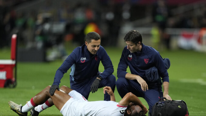 El delantero del Sevilla Chidera Ejuke (tumbado) es atendido por los servicios médicos del equipo, durante el partido de LaLiga que el Barcelona y el Sevilla disputaron este domingo en el estadio Lluis Companys. EFE/Alejandro García
