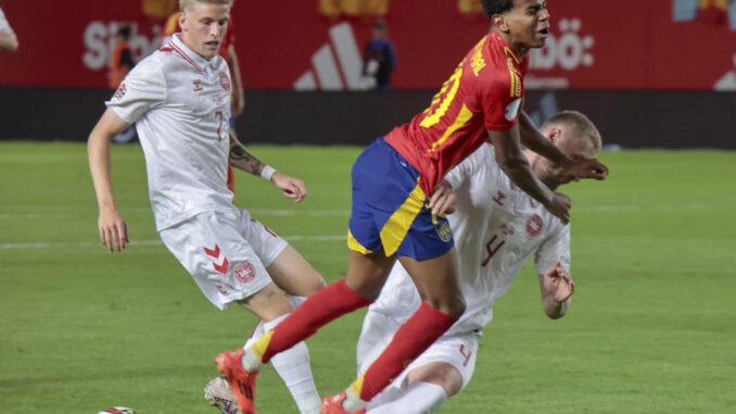 El delantero de la selección española, Lamine Yamal (c), cae ante la entrada del defensor de Dinamarca durante el encuentro correspondiente a la fase de grupos de la Liga de Naciones que disputaron España y Dinamarca en el estadio Enrique Roca de Murcia. EFE / Juan Carlos Caval.
