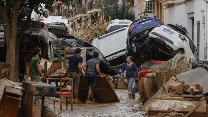 Vecinos de Paiporta trabajan en la limpieza de calles, locales y viviendas de la localidad junto a una montaña de vehículos arrastrados por la corriente, este viernes, en la provincia de Valencia (España). EFE/Biel Aliño
