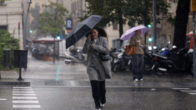 Una mujer se protege de la lluvia en el centro de Barcelona este lunes cuando las comarcas de del Garraf y del Barcelonès, en Barcelona, están en aviso rojo de la Agencia Estatal de Meteorología (Aemet), y la Generalitat ha enviado una alerta a los teléfonos móviles por la llegada de lluvias continuadas y torrenciales. EFE/Alberto Estévez
