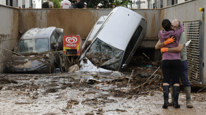 Dos vecinos se abrazan a la entrada de un garaje en Paiporta, Valencia, tras el paso de la DANA. EFE/Biel Aliño
