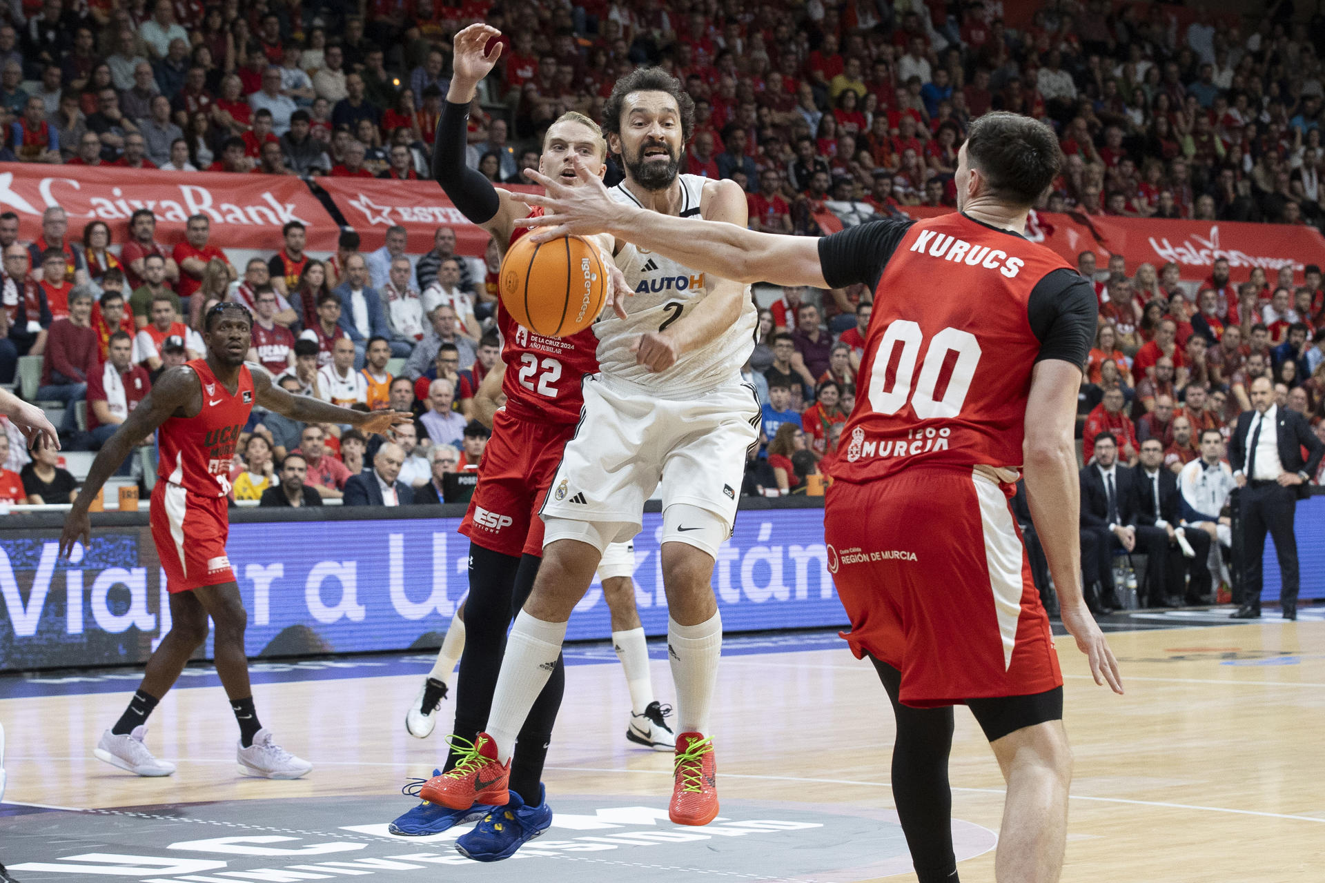 El escolta del Real Madrid Sergio Llull (c) pasa el balón a un compañero ante la presión del base sueco de UCAM Murcia Ludde Hakanson (i), durante el partido de la sexta jornada de la liga Endesa jugado en el Palacio de los Deportes de Murcia. EFE/Marcial Guillén
